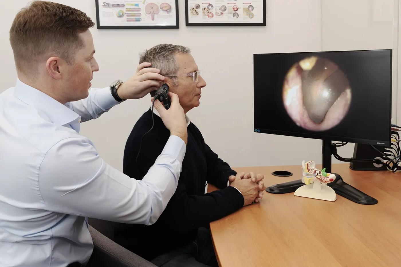 An audiologist examining a patient's ear, with the view on screen