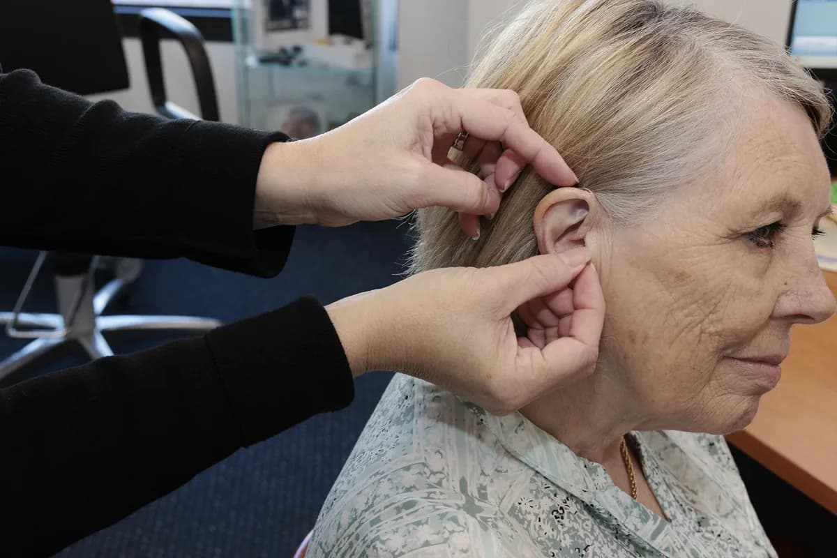 A clinician fitting a hearing aid behind a patient's ear.